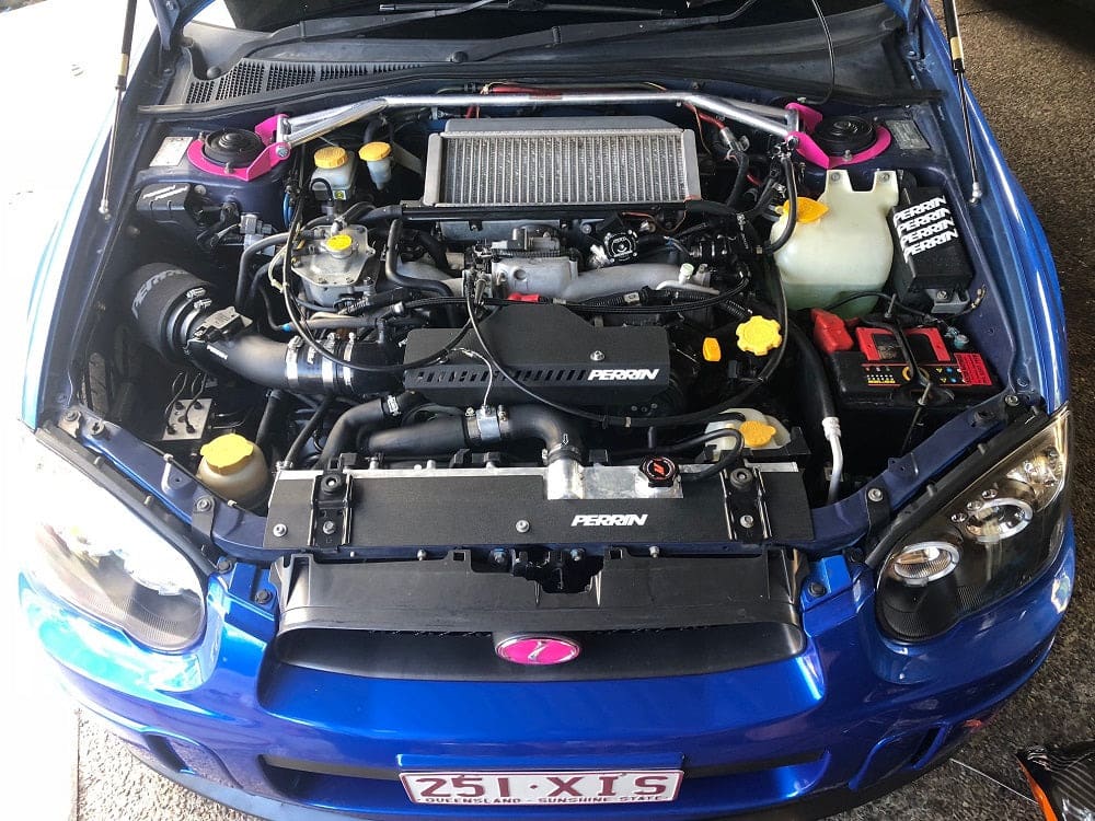Blue Subaru WRX engine bay with a top mount intercooler, Perrin hoses and a front strut brace